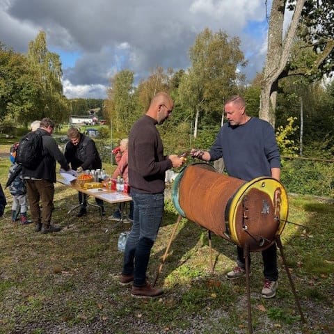 En man står bakom en tunngrill och serverar korv till en annan man.