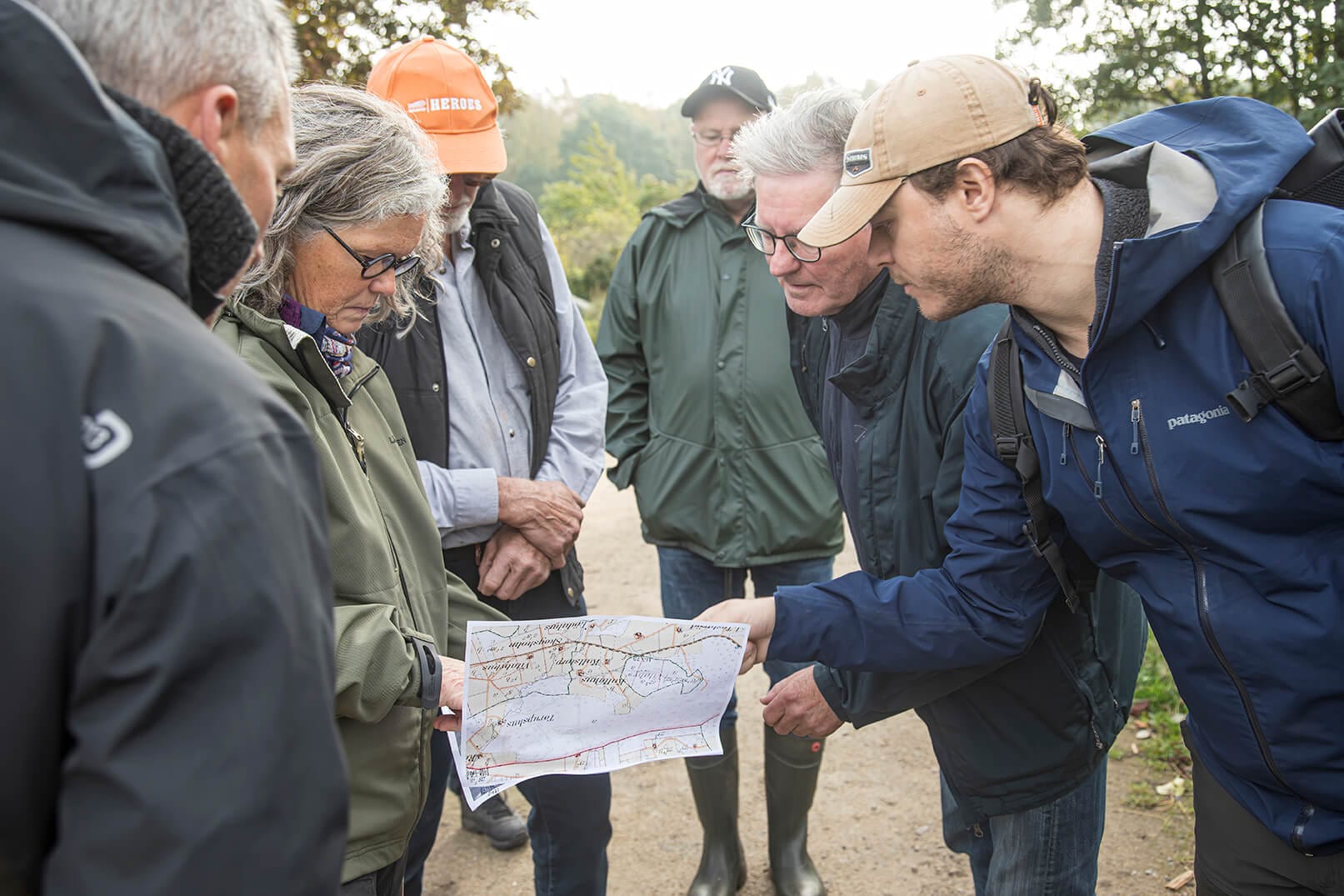 Människor samlade runt en karta i naturmiljö, diskuterar rutt eller område under en gemensam exkursion
