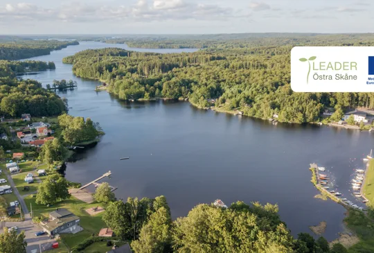 Flygvy över sjön Immeln med skog, bebyggelse, bryggor och småbåtshamn i ett naturskönt landskap.