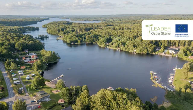 Flygvy över sjön Immeln med skog, bebyggelse, bryggor och småbåtshamn i ett naturskönt landskap.
