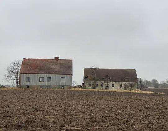 Två förfallna ödehus bredvid varandra i horisonten på vid en åkermark