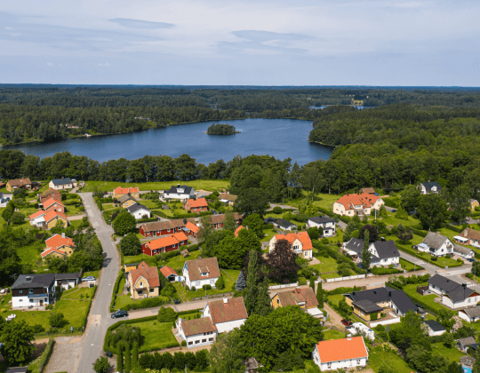 Flygbild över småhusområde nära sjö och skog i Hässleholms kommun, som visar en typisk stationsortsmiljö
