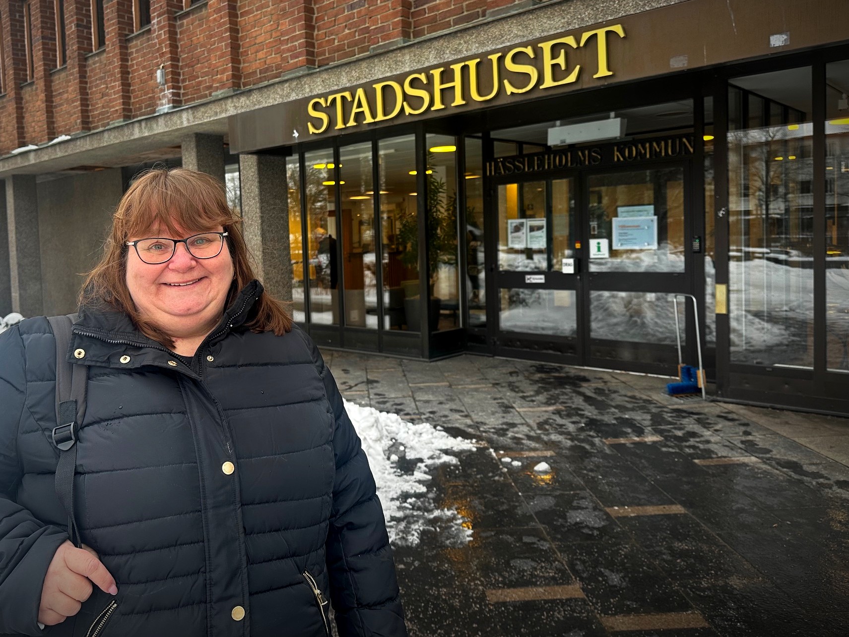 Kvinna i svart jacka står utanför Stadshuset i Hässleholm, med snö på marken och entrén synlig i bakgrunden