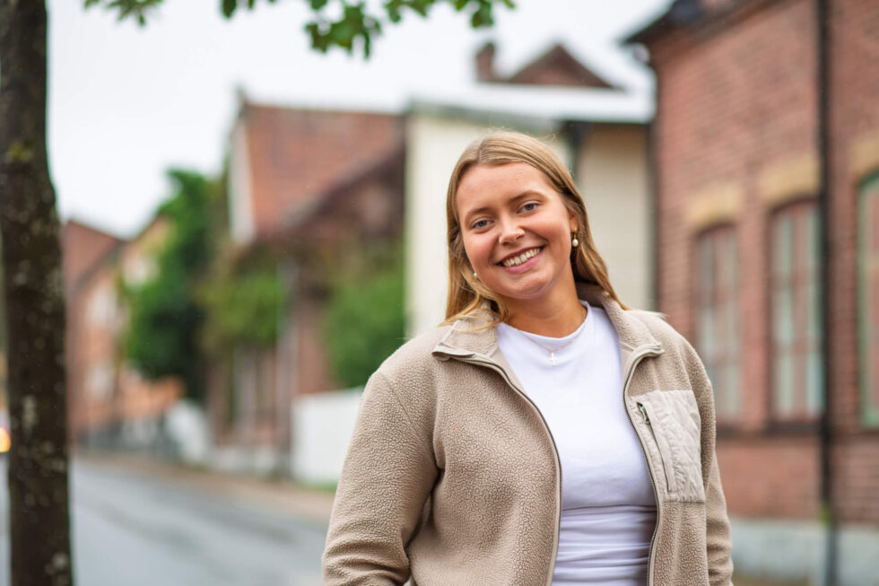 Emma Ernstsson, projektledare för Levande stationsorter, ler mot kameran med tegelbyggnader i bakgrunden.